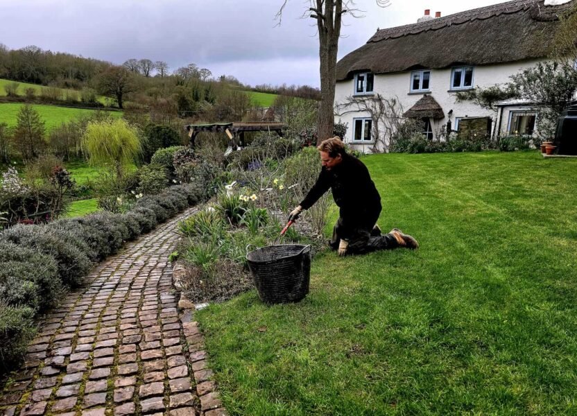 Dan weeding in front of a rustic cottage